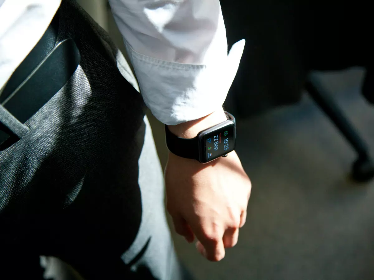 A person's wrist with a black Apple Watch on it. The watch face shows the time. The background is blurred, making the watch the main focus.